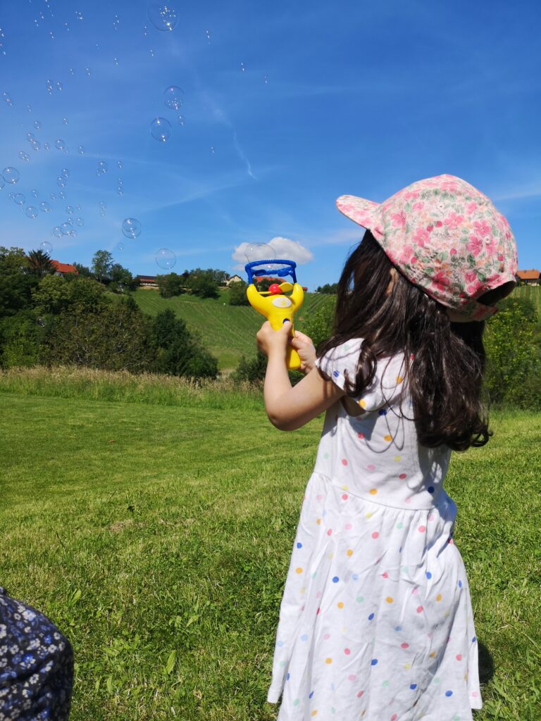 Kind macht Seifenblasen auf grüner Wiese